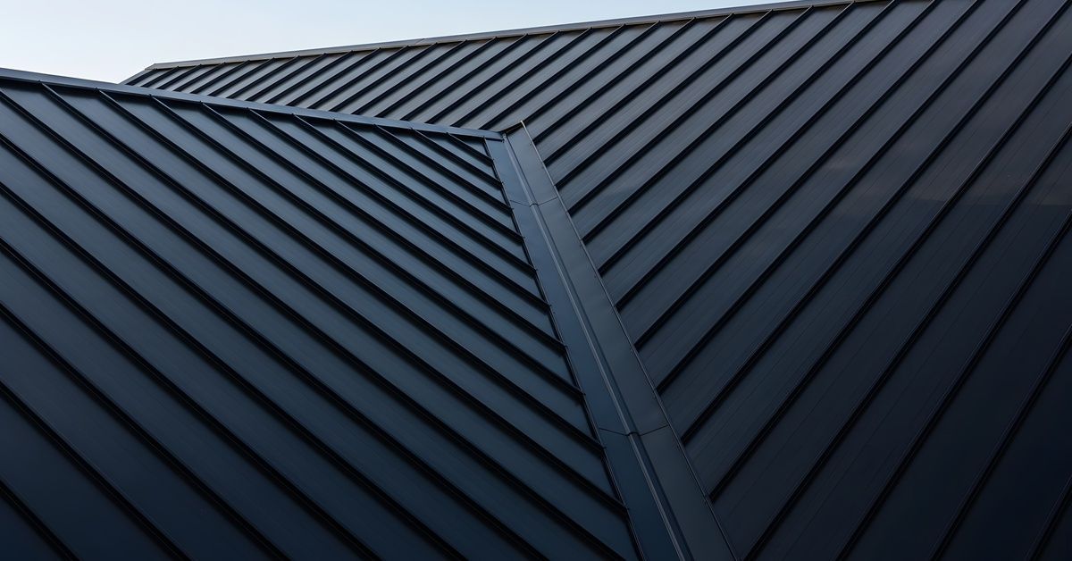 Black metal roof panels form sharp angles where two sloped sections come together. The roof has standing seams.