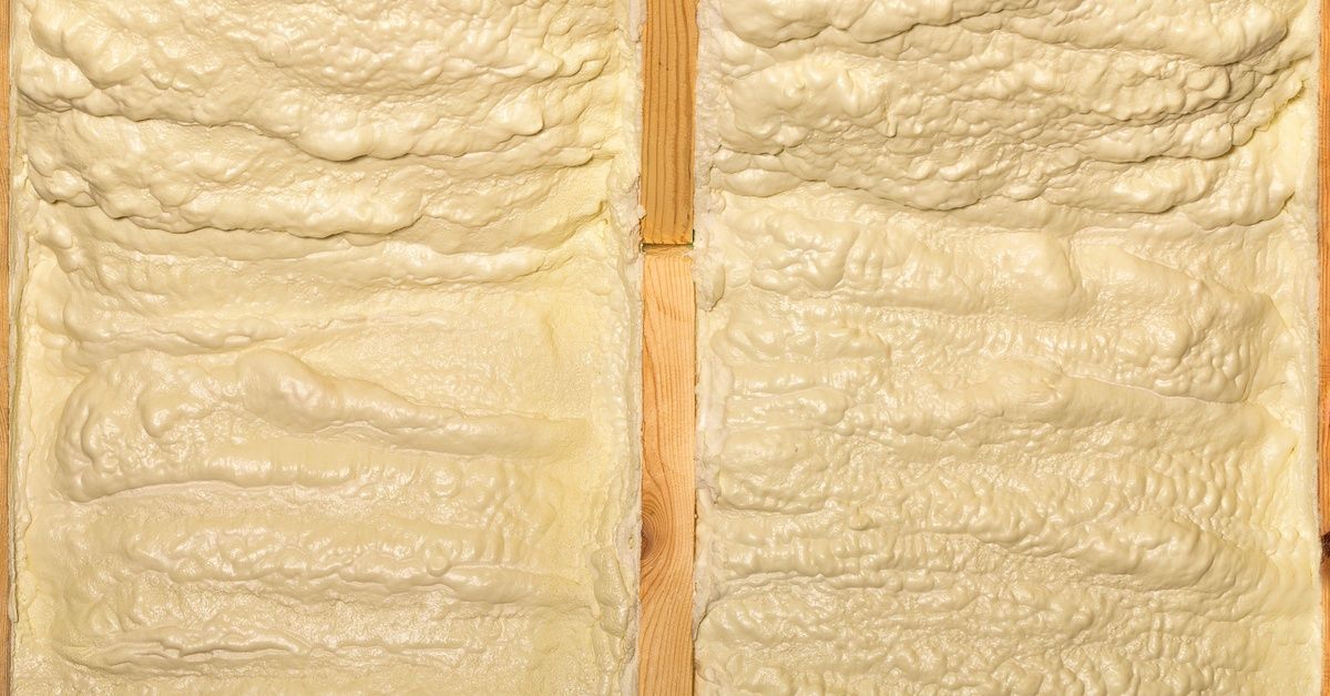 Pale yellow spray foam fills two wall cavities separated by a vertical wood stud. The foam has a bumpy texture.