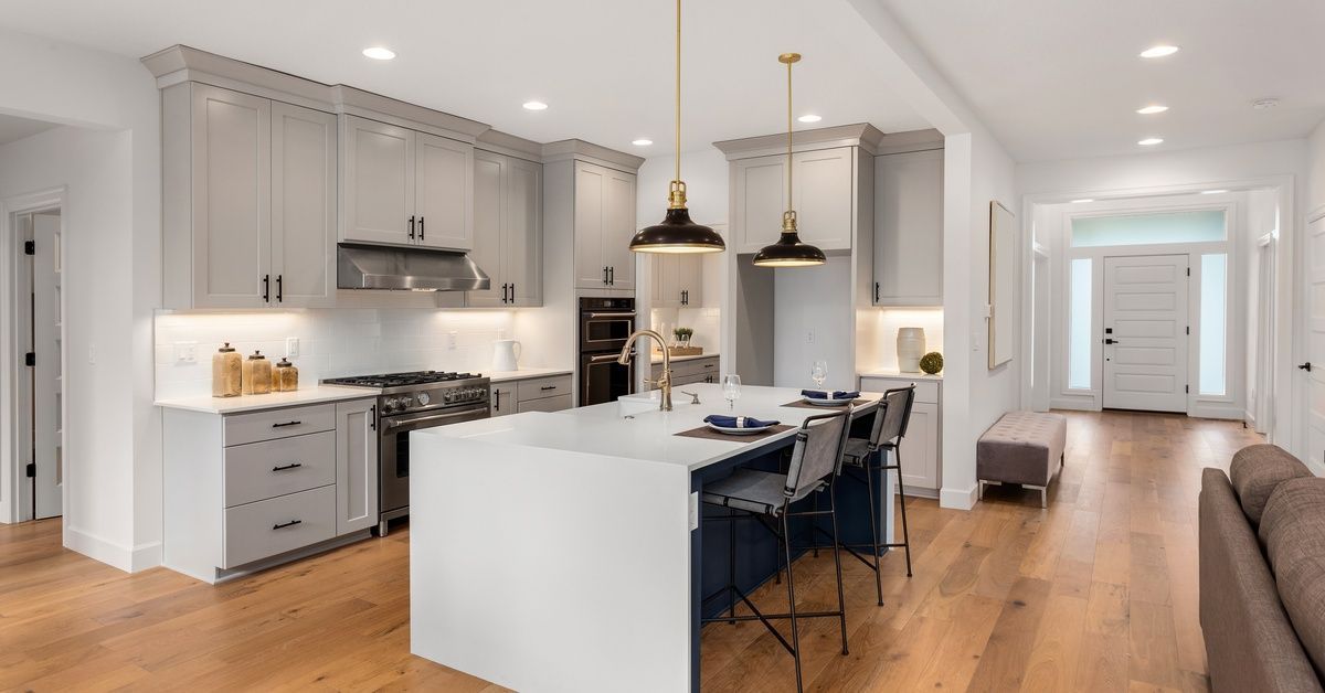 A kitchen with shaker cabinets and an island features recessed lights, two black pendants, and under-cabinet lighting.
