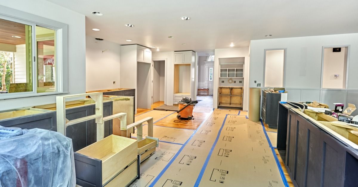 A partially renovated kitchen has dark lower cabinets, unfinished counters, and protective paper covering the floor.