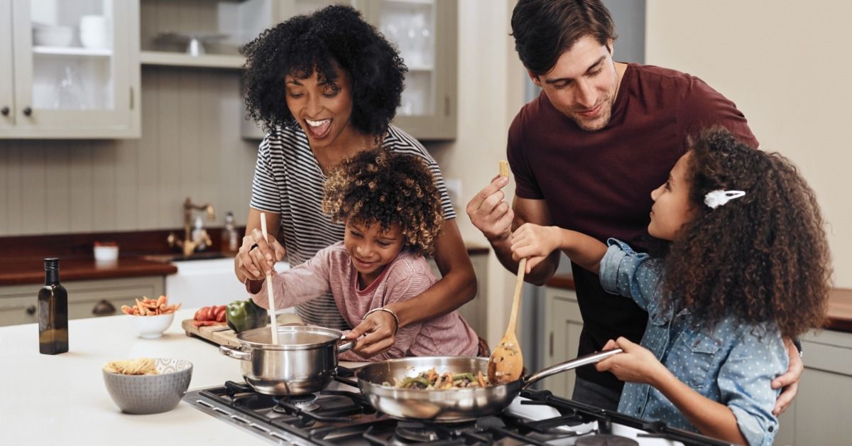 A family cooks together around a stovetop built into a large kitchen island.