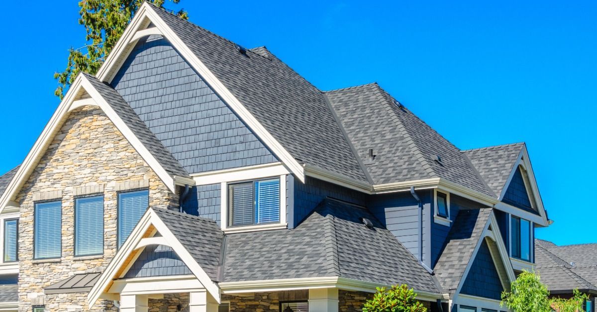 A large two-story home has multiple steep, gabled rooflines covered with gray asphalt shingles.