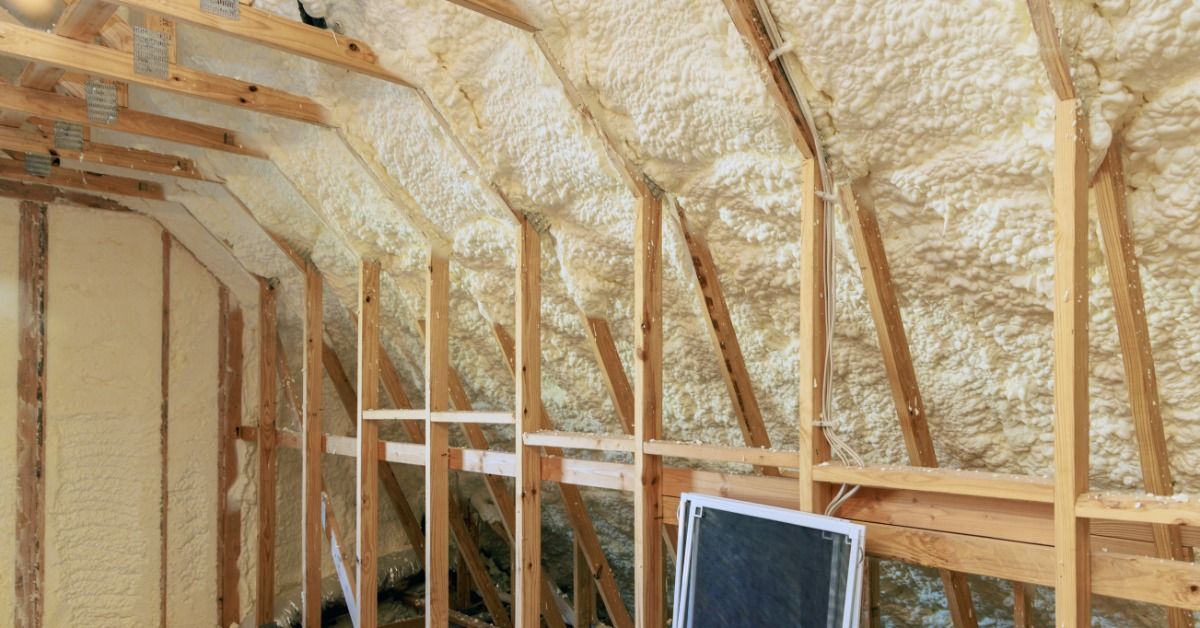 Spray foam insulation fills the spaces between exposed wooden rafters and wall studs in an unfinished attic.