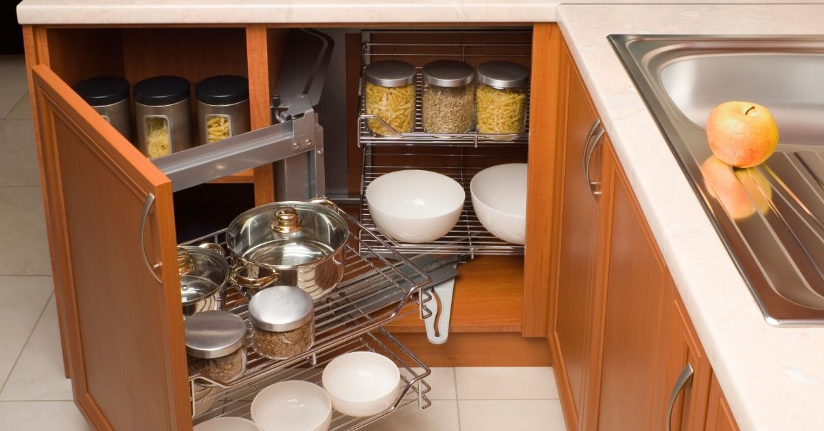 A wooden corner kitchen cabinet features pull-out metal shelves holding pots, bowls, and food storage jars.
