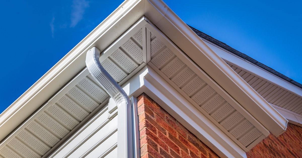 A gutter system follows the roofline of a brick and siding house, with a downspout at the corner.