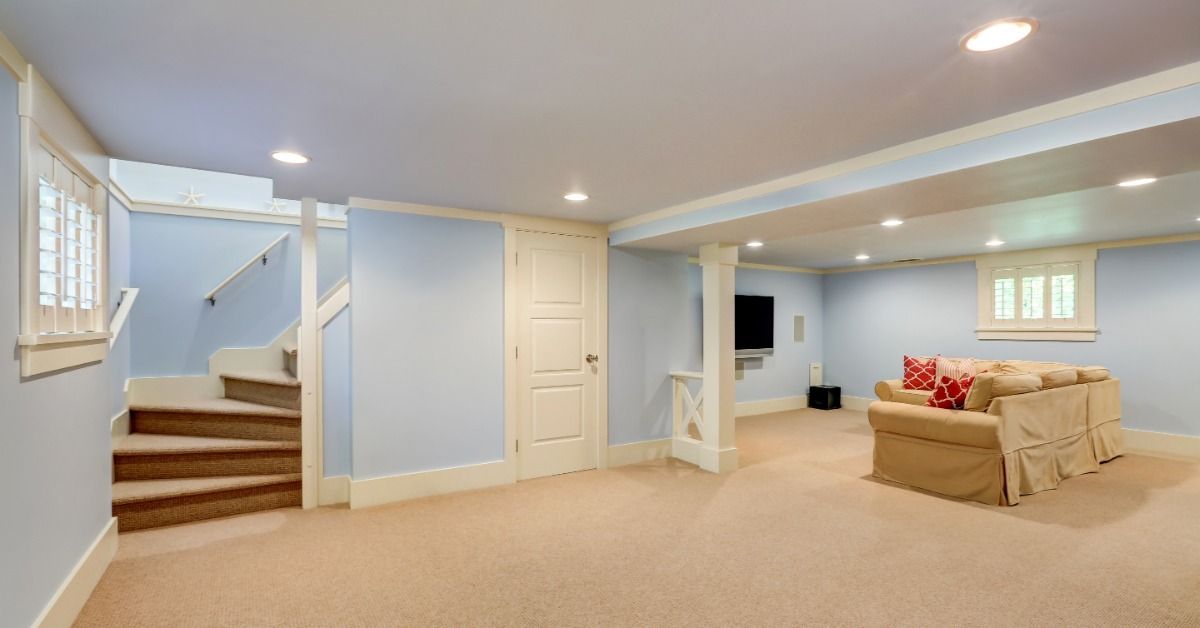 A sofa sits near a television in a finished basement with light blue walls, beige carpeting, and rec
