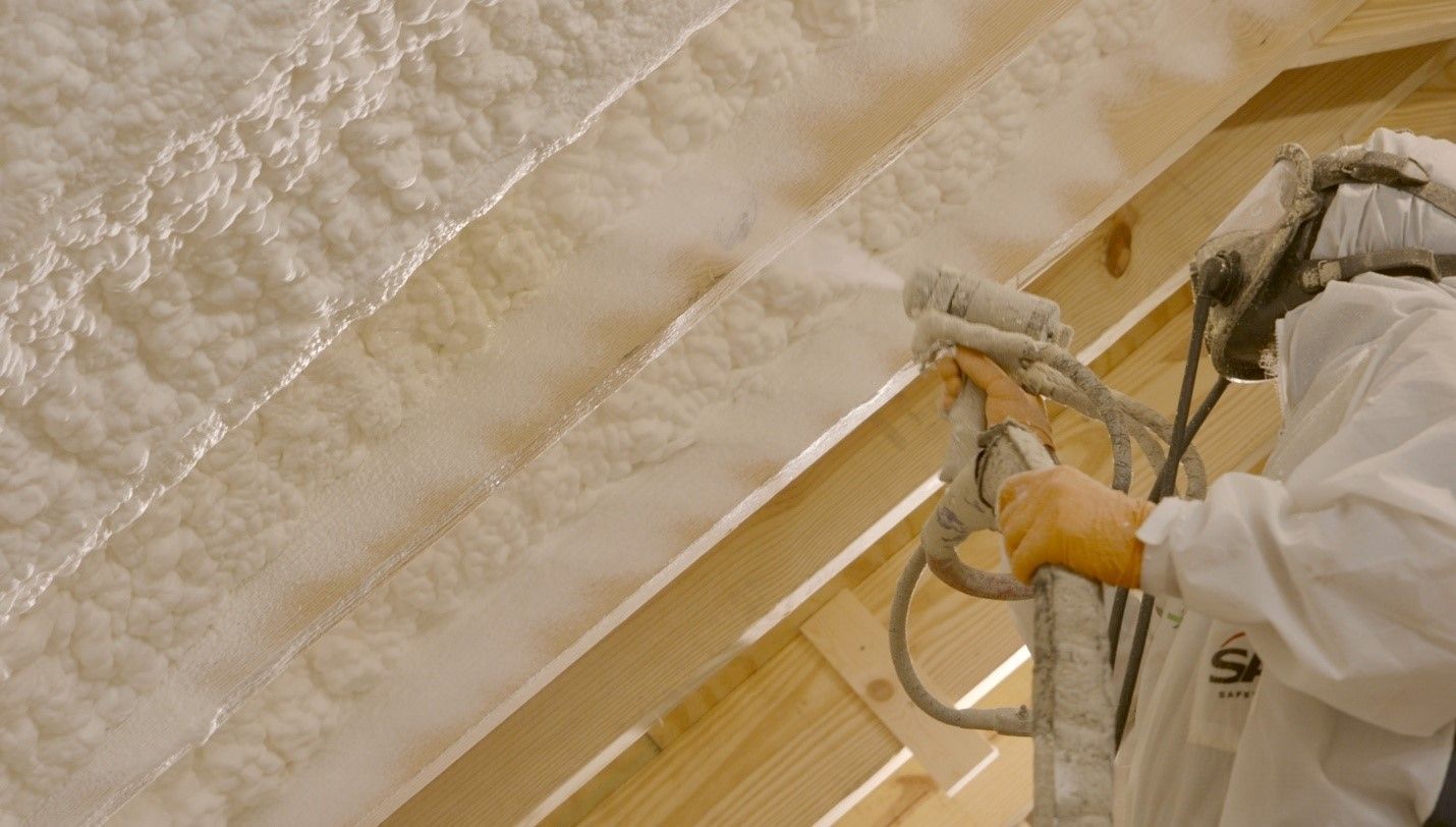 A person is spraying foam on the ceiling of a building.
