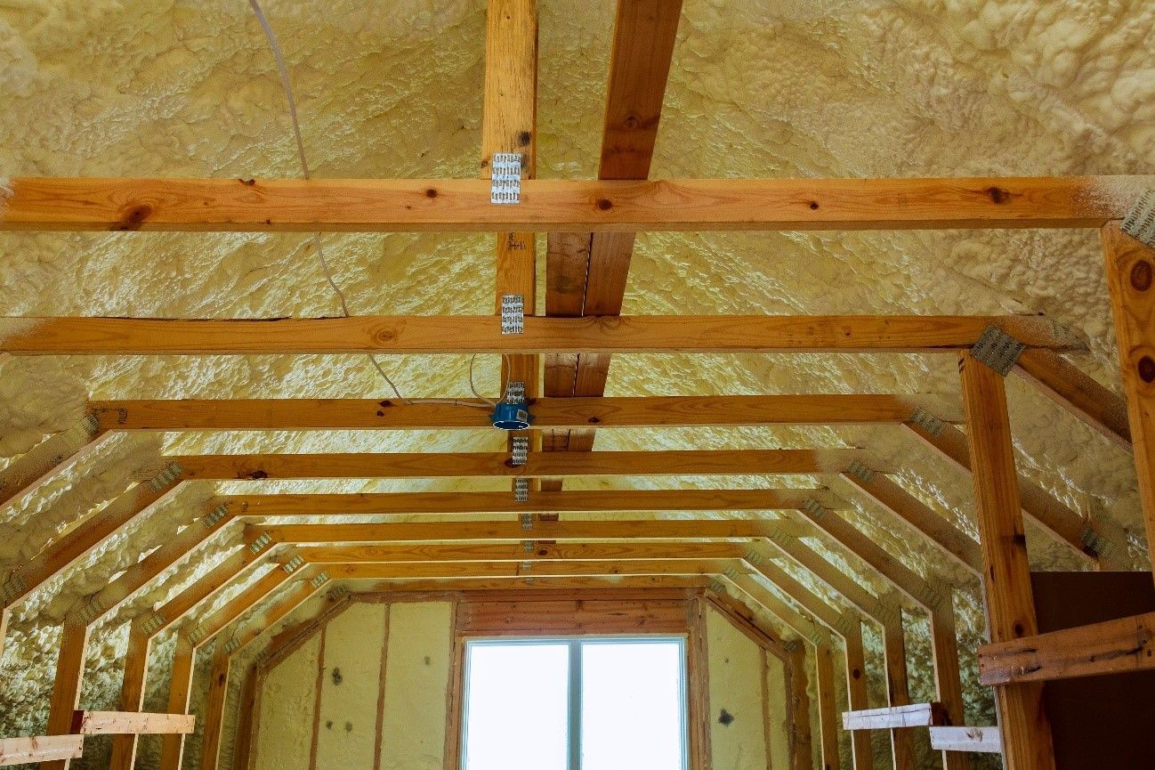 The ceiling of an attic with wooden beams and insulation.