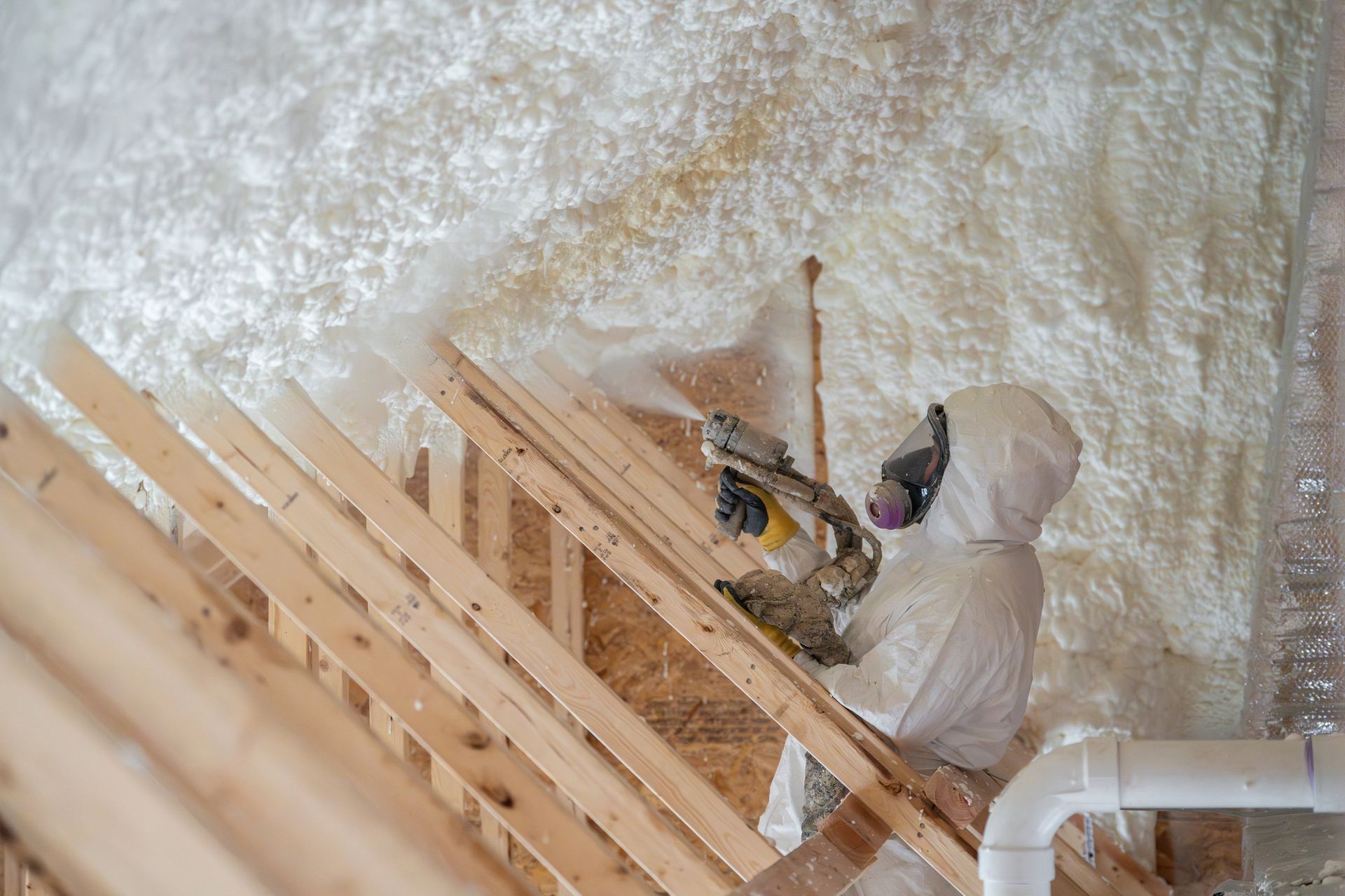 A man is spraying insulation on the ceiling of a house under construction.