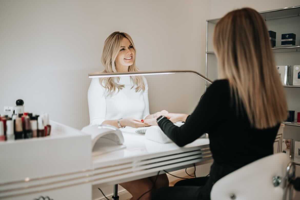 Kundin und Nageldesignerin an einem Maniküreplatz mit Weißlichtlampe, die sich in einem Salon