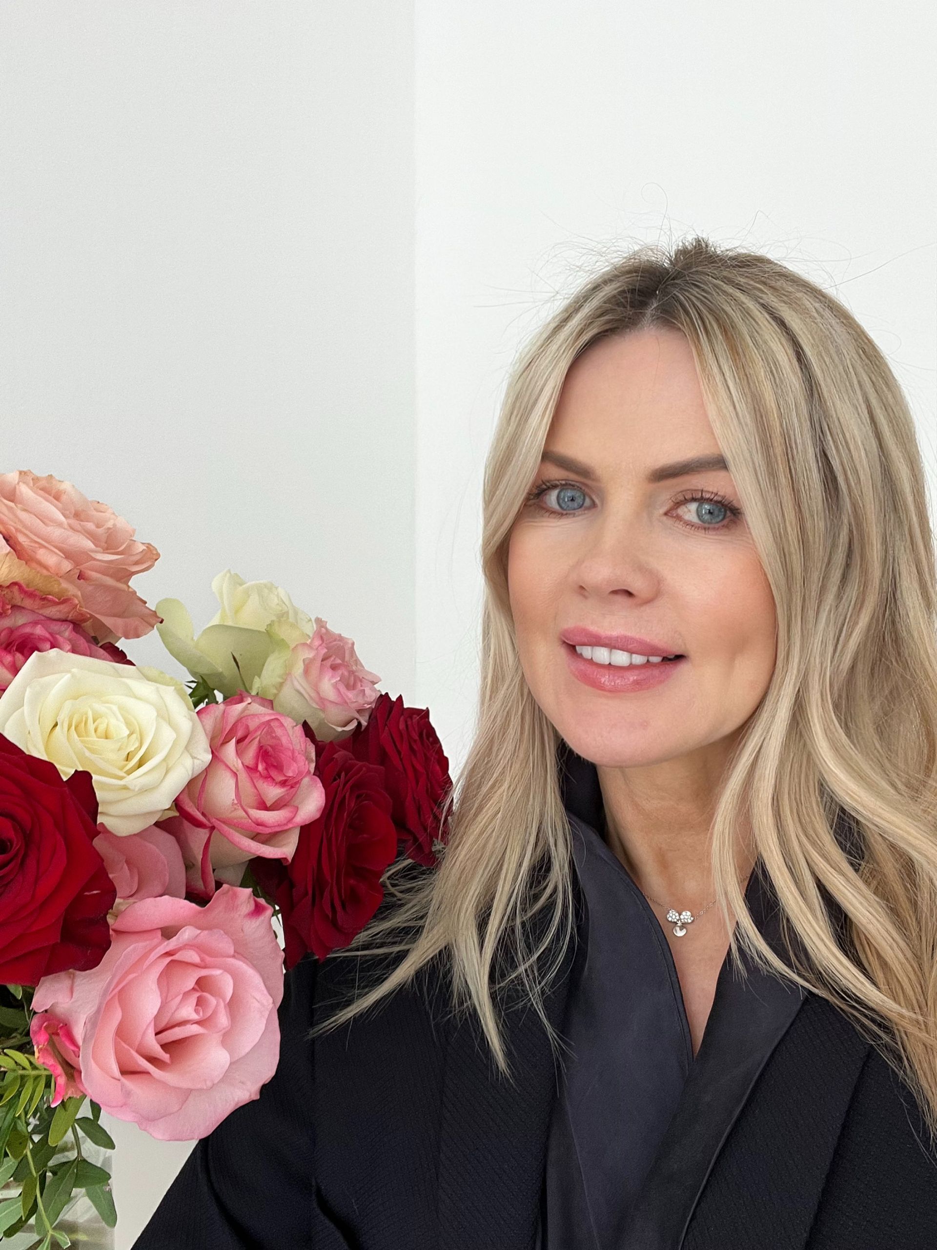 Frau lächelt neben einem Strauß roter, rosa und weißer Rosen in einem hellen Raum
