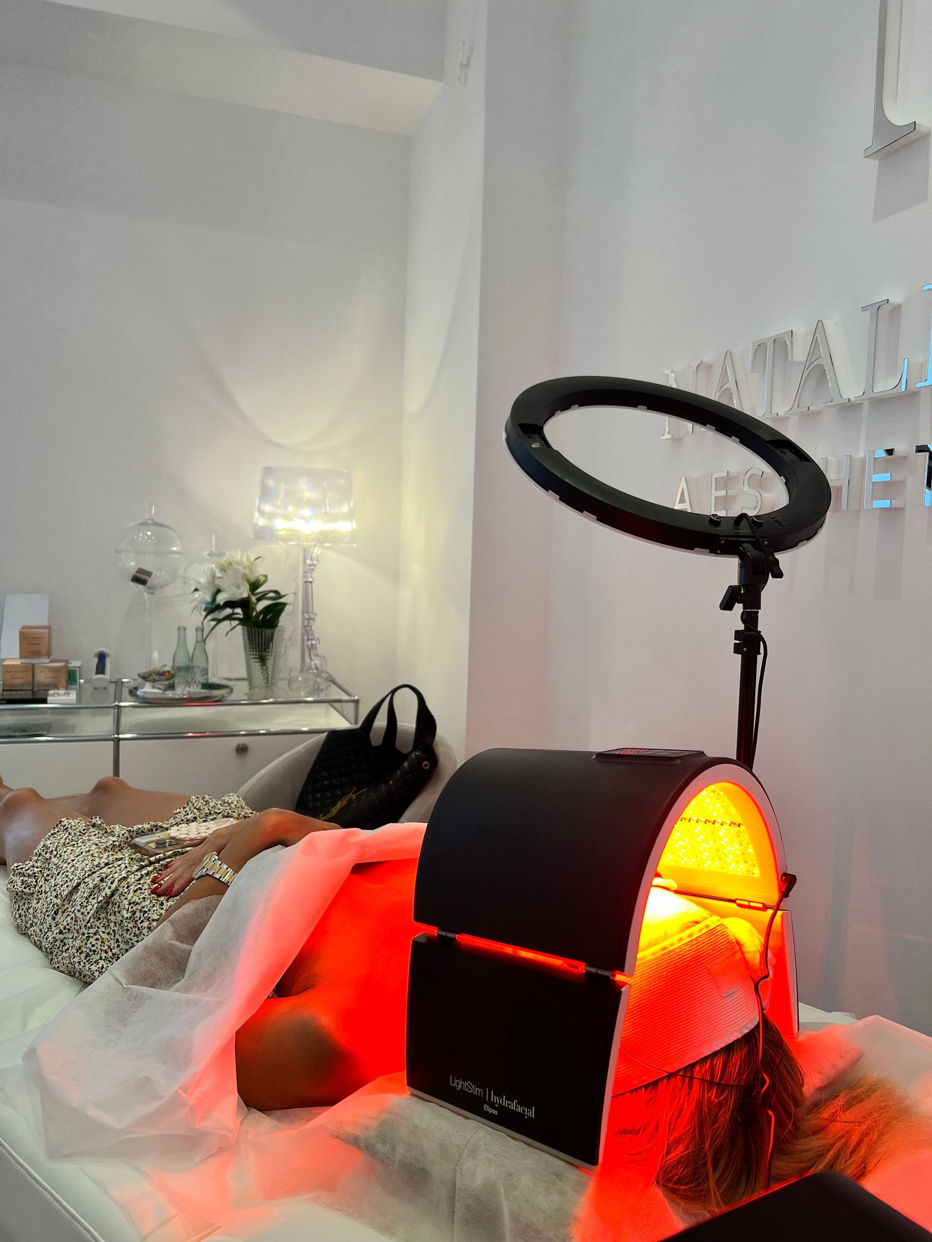Eine Schlafzimmerszene mit einem leuchtend roten Infrarot-Therapiegerät neben einem Bett und einem Ringlicht.