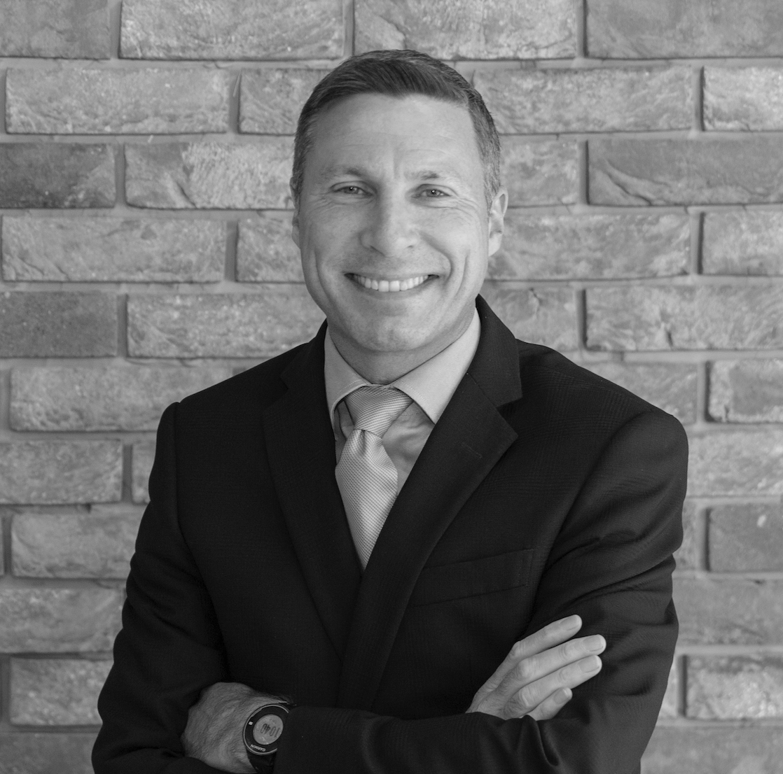 Mark Johnson, the founder, in a suit with arms crossed, standing in front of a brick wall.