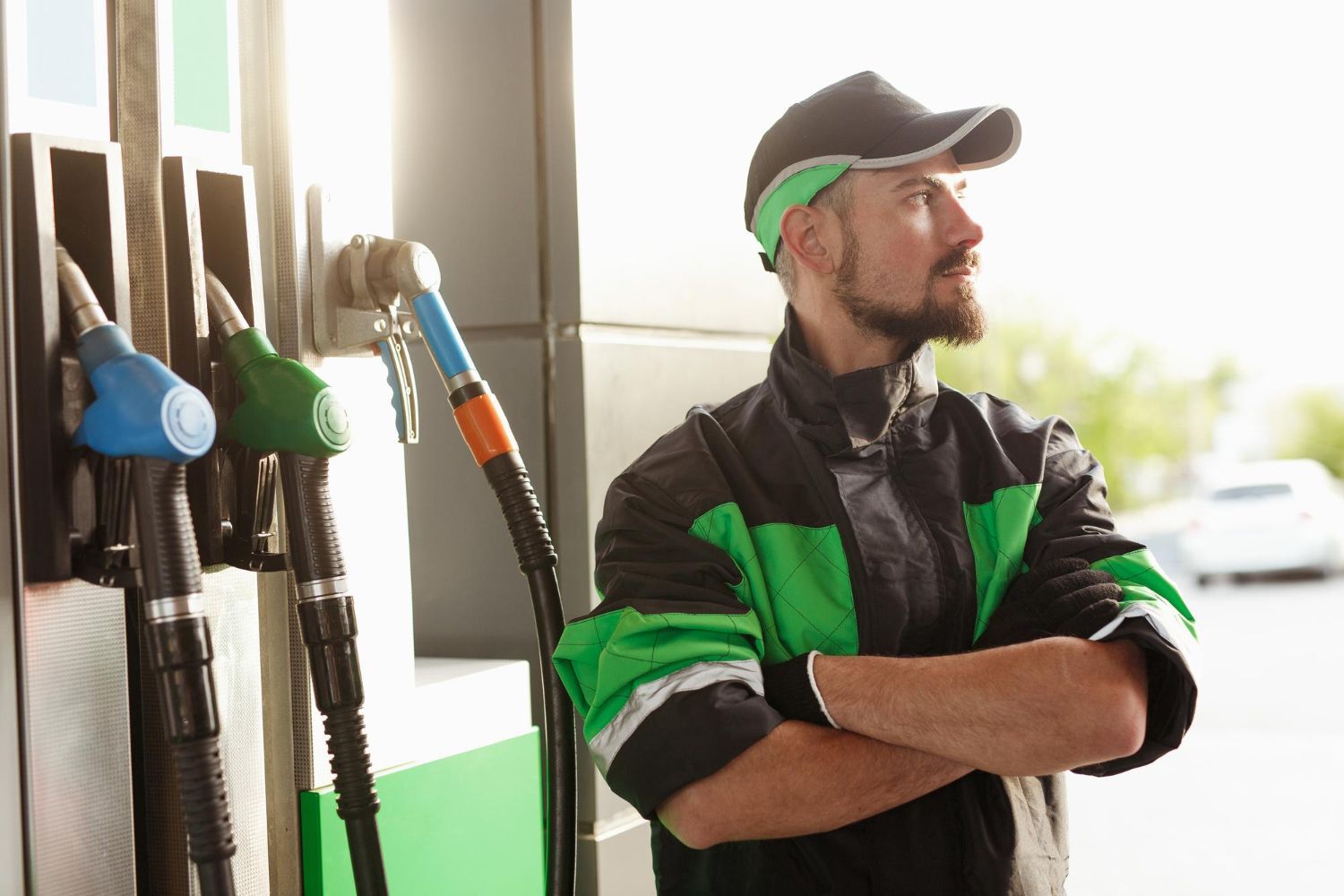 Frentista de posto de gasolina com os braços cruzados, ao lado das bombas de combustível.