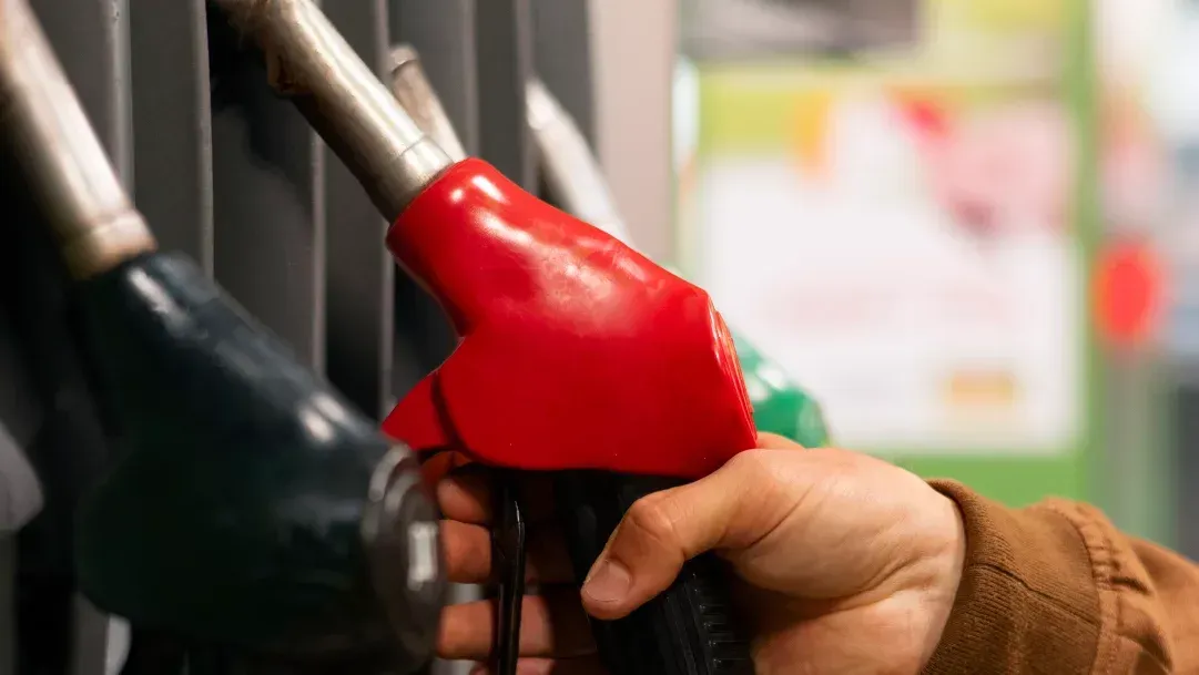 Uma pessoa está segurando uma bomba de gasolina na mão em um posto de gasolina.