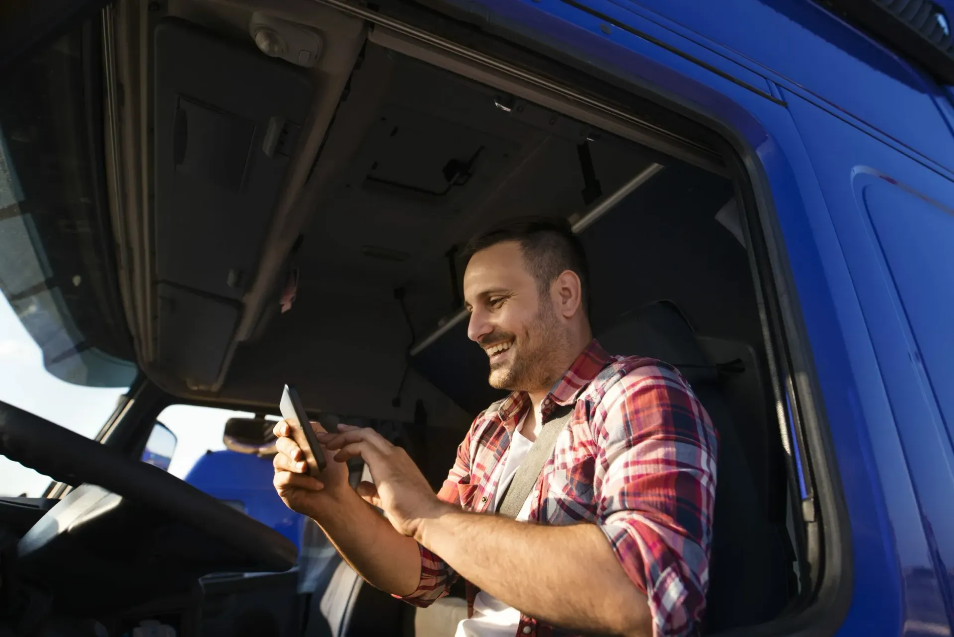 Um homem está sentado no banco do motorista de um caminhão azul usando um telefone celular.