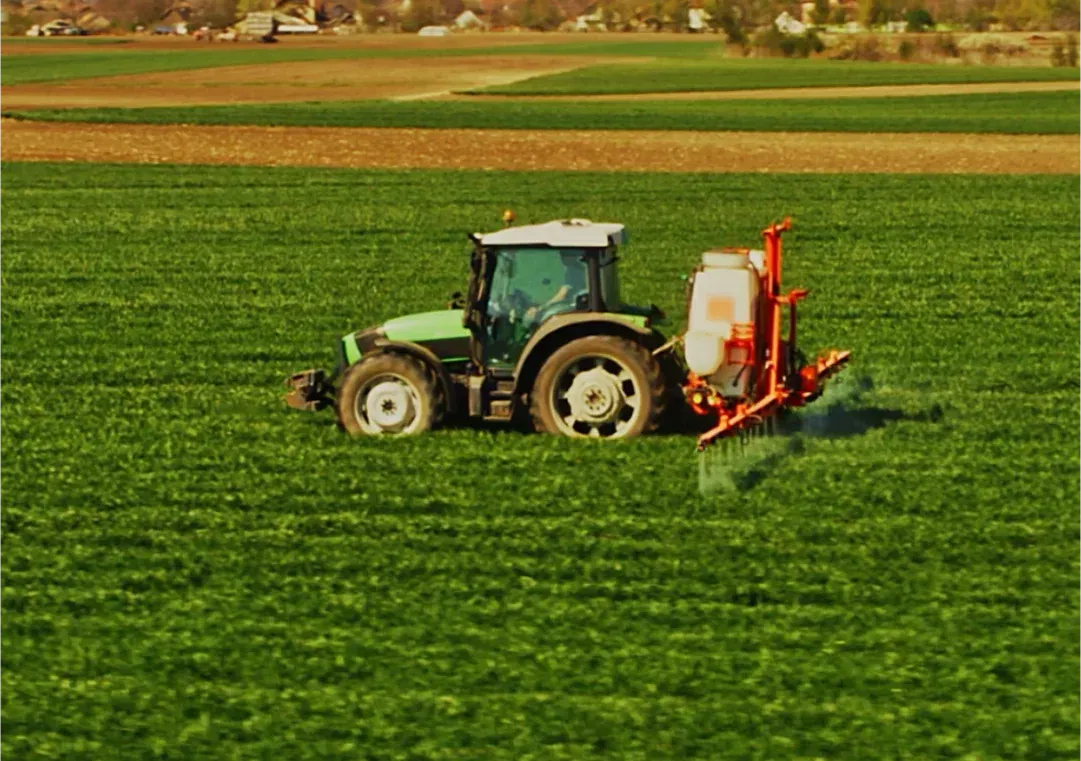 Um trator verde está pulverizando fertilizante em um campo verdejante.