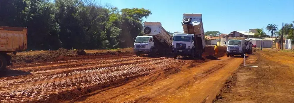 Uma fileira de caminhões basculantes está descendo uma estrada de terra.