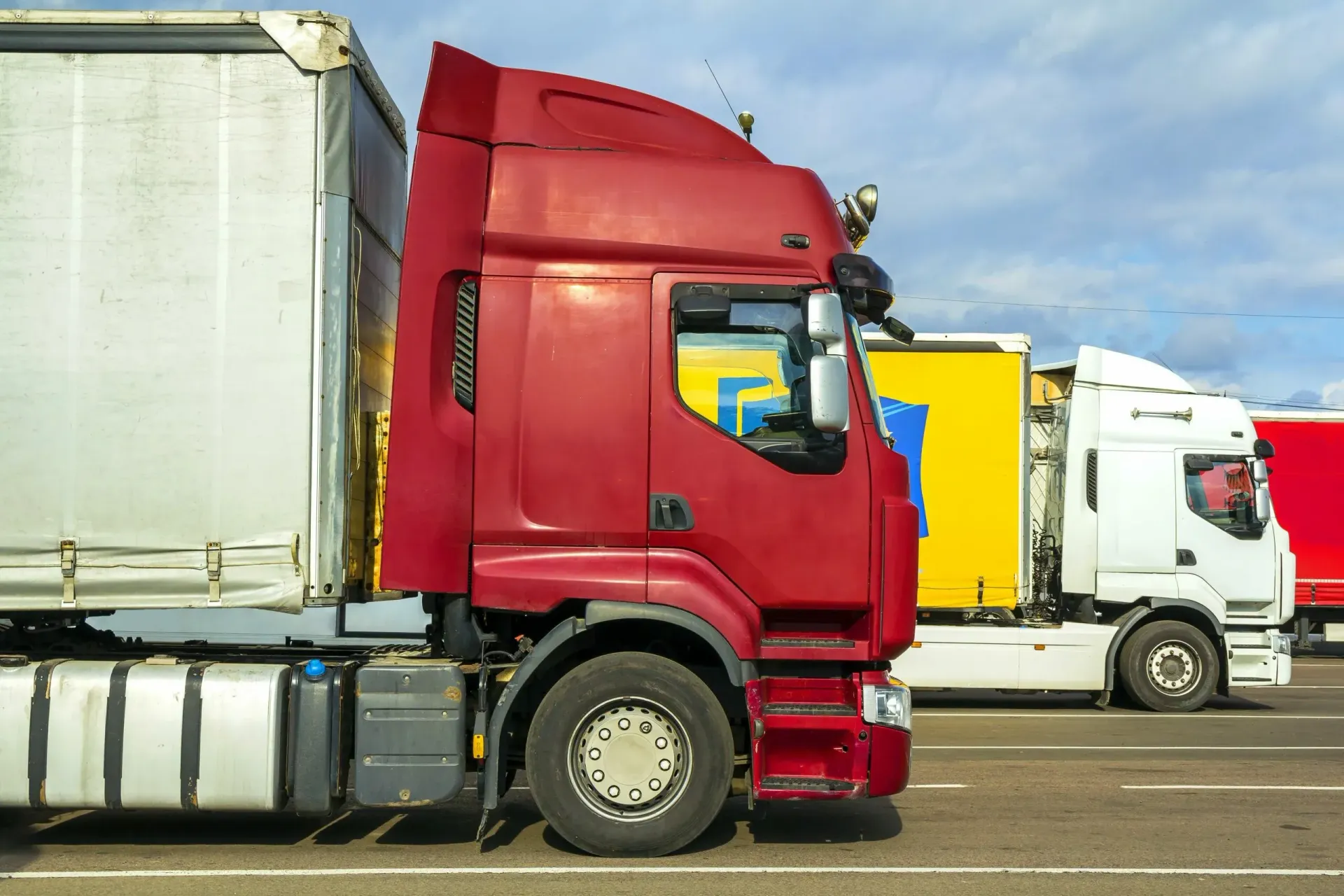 Uma fileira de caminhões semirreboques estão estacionados em um estacionamento.