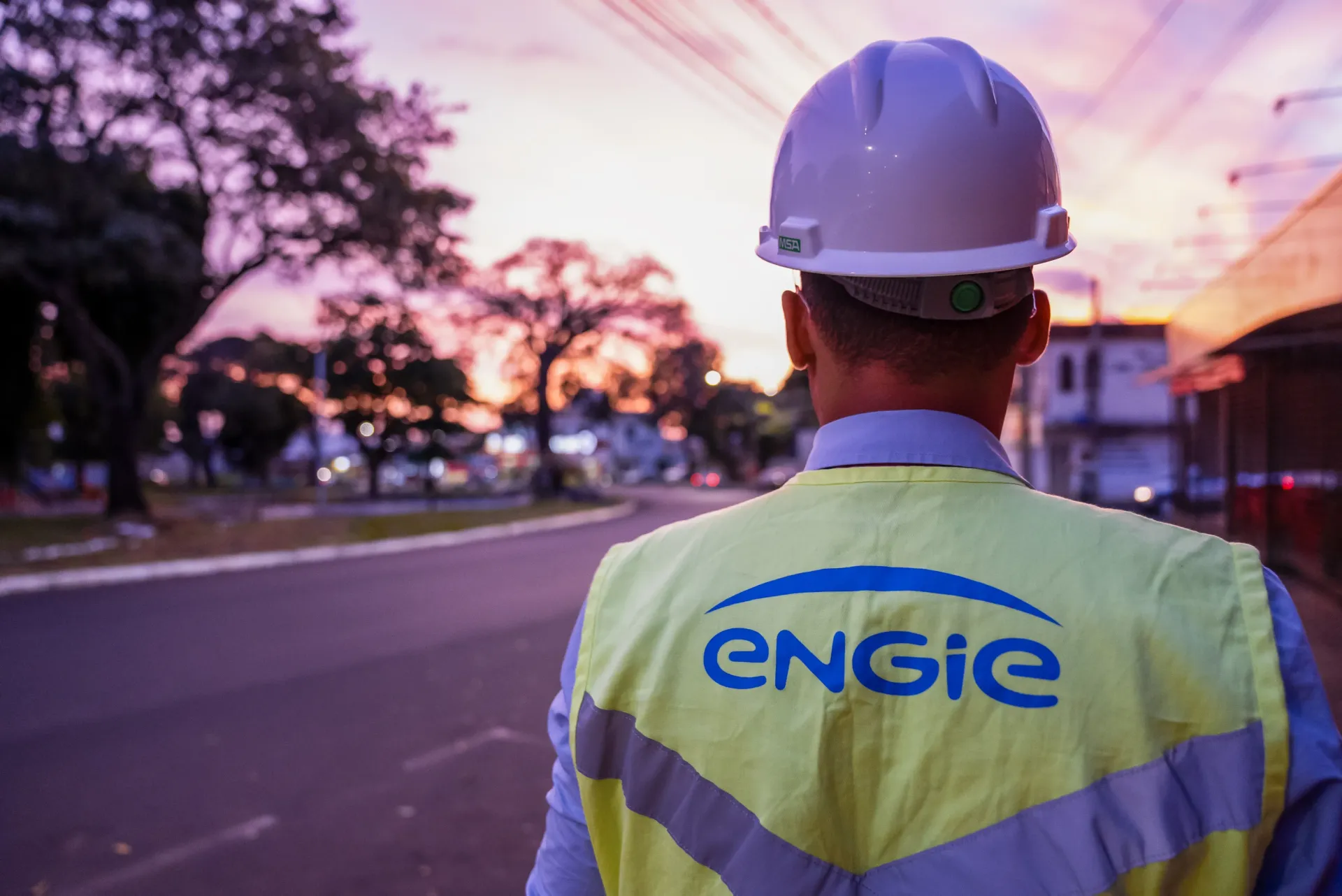 Operário com colete com o logotipo da ENGIE caminhando pela rua ao entardecer.