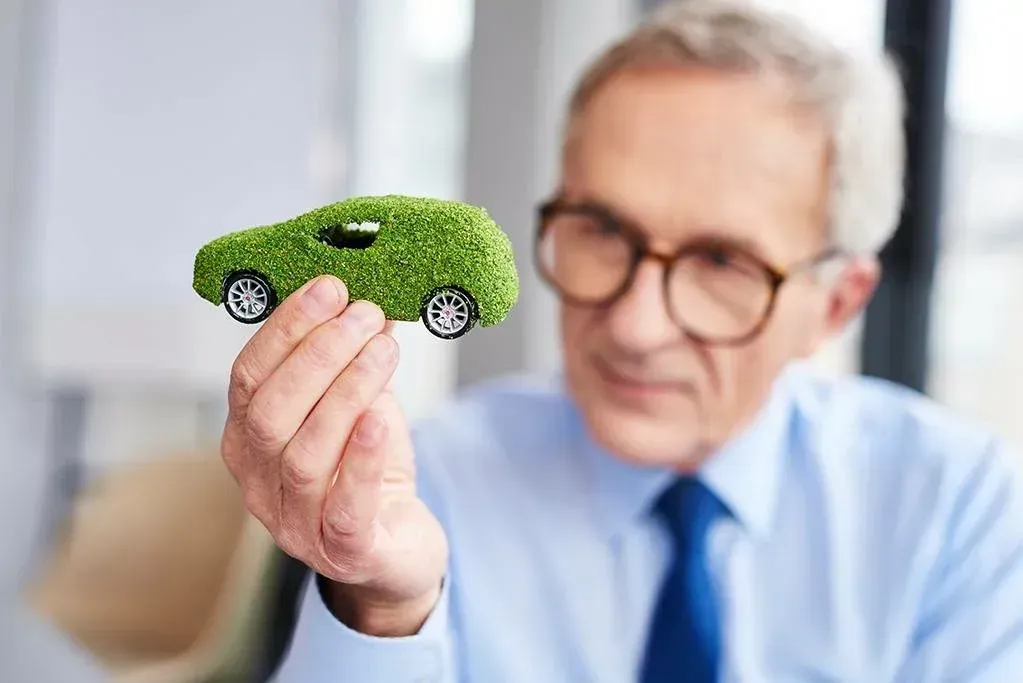 Um homem está segurando um carro verde feito de grama.