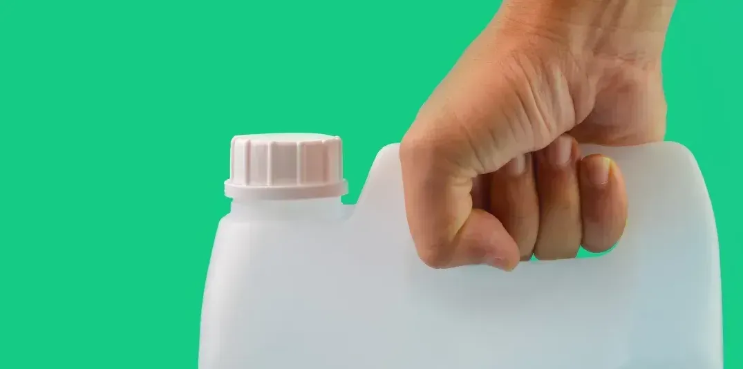 Uma mão segura uma garrafa de plástico sobre um fundo verde.