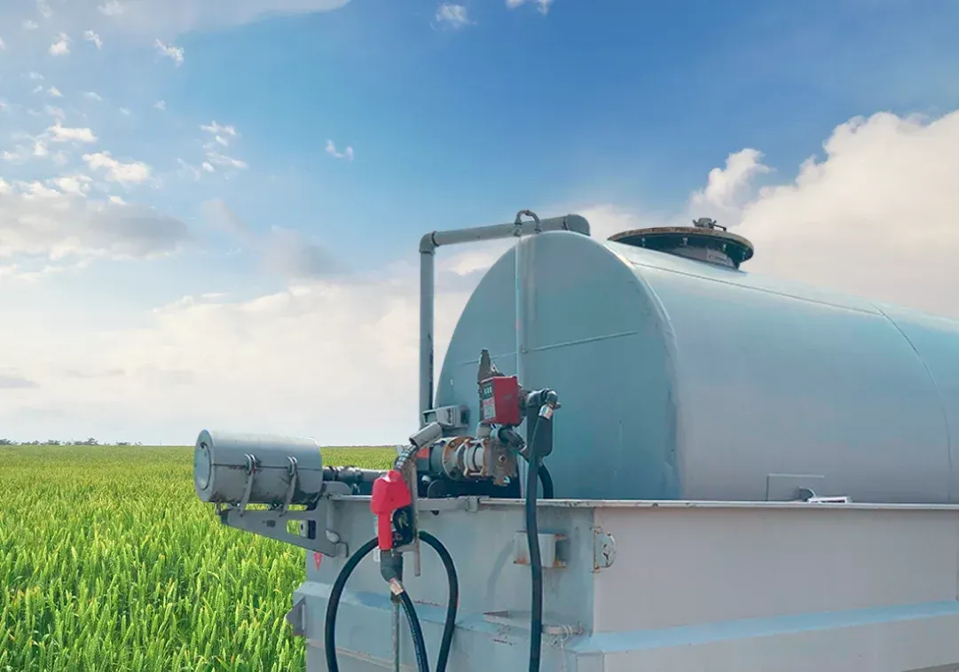 Tanque branco com bomba de combustível em um campo de plantações verdes sob um céu azul.
