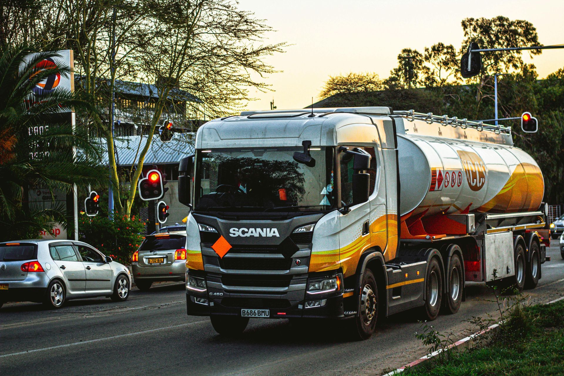 Caminhão comboio de combustível laranja e branco trafegando em uma rua da cidade ao entardecer