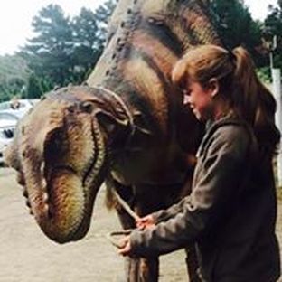 A woman is standing next to a statue of a dinosaur.