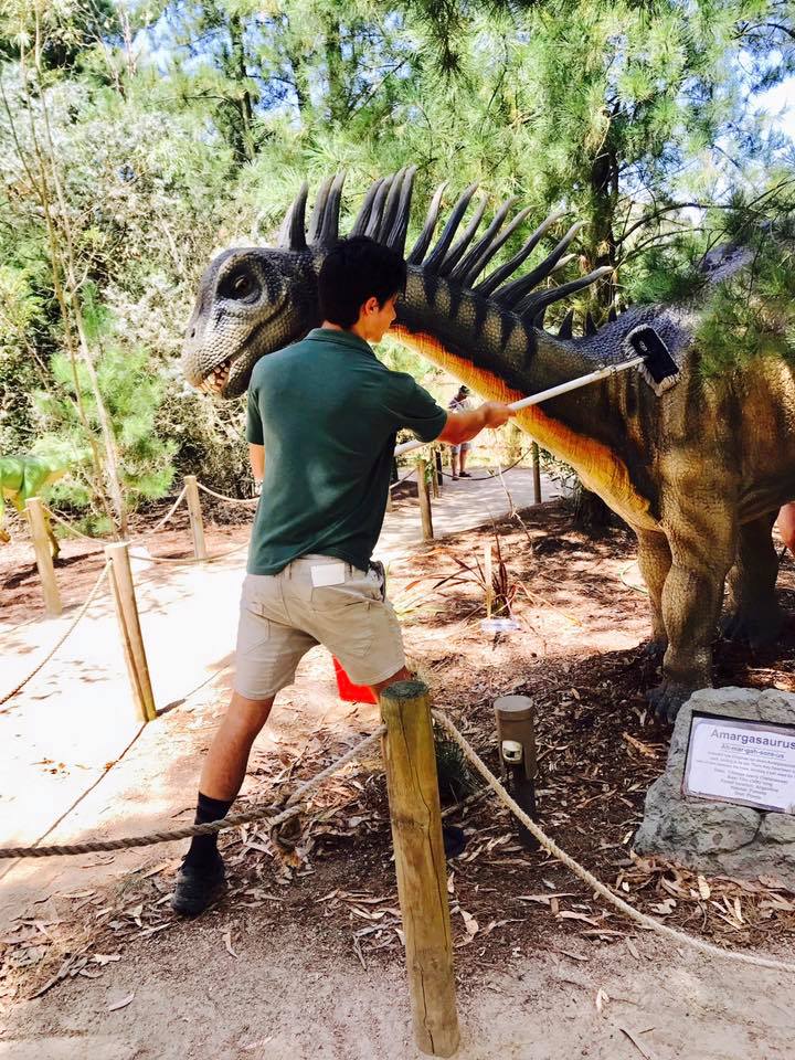 A man is standing next to a statue of a dinosaur.