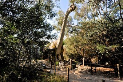 A large dinosaur statue is standing in the middle of a forest.