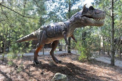 A dinosaur statue is standing in the middle of a forest.