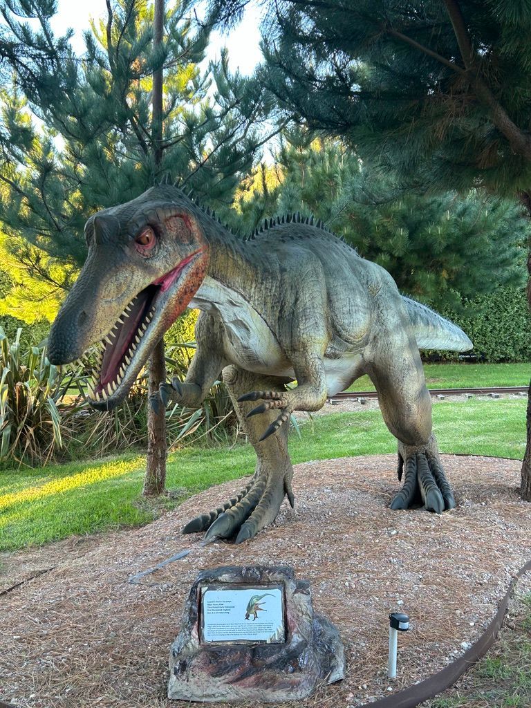 A statue of a dinosaur is standing in a park.