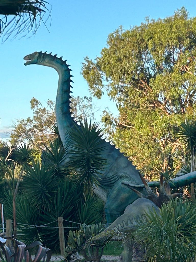 A large dinosaur statue is surrounded by trees in a park.