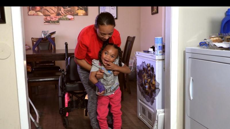 Adult helping child stand in a kitchen
