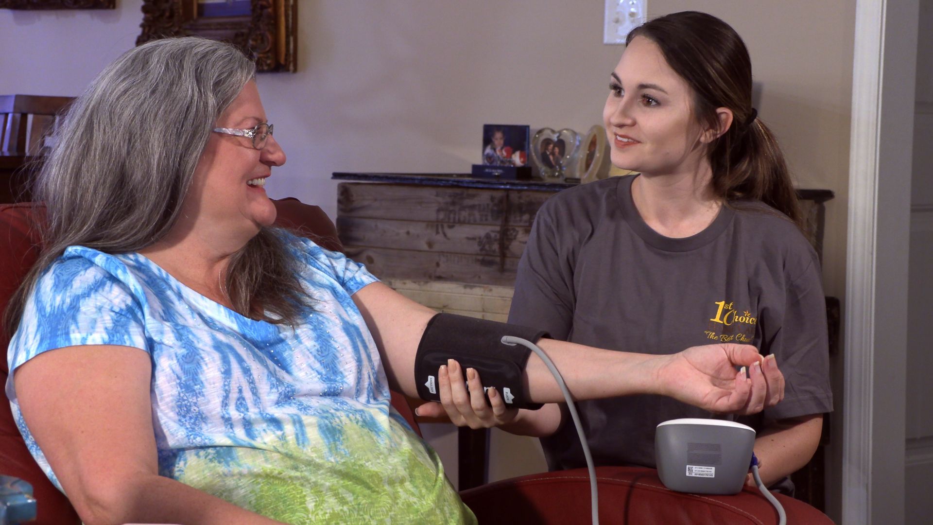 Woman checks another woman’s blood pressure while seated indoors on a couch.