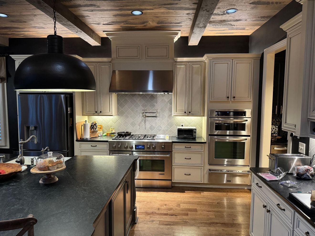 Kitchen with stainless steel appliances, distressed white cabinets, dark island, and wood ceiling.