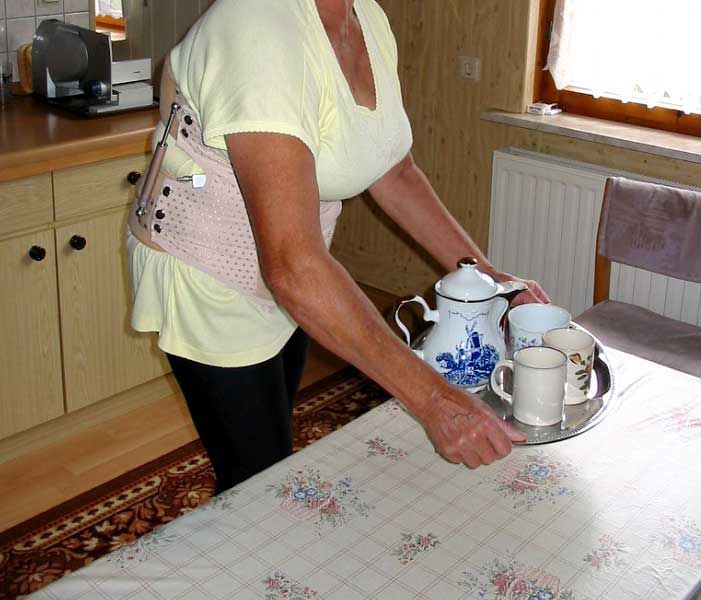 Eine Frau in Orthese hält ein Tablett mit Teekannen und Tassen darauf
