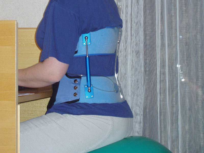 Eine Frau in einer blauen Orthese sitzt auf einem grünen Ball