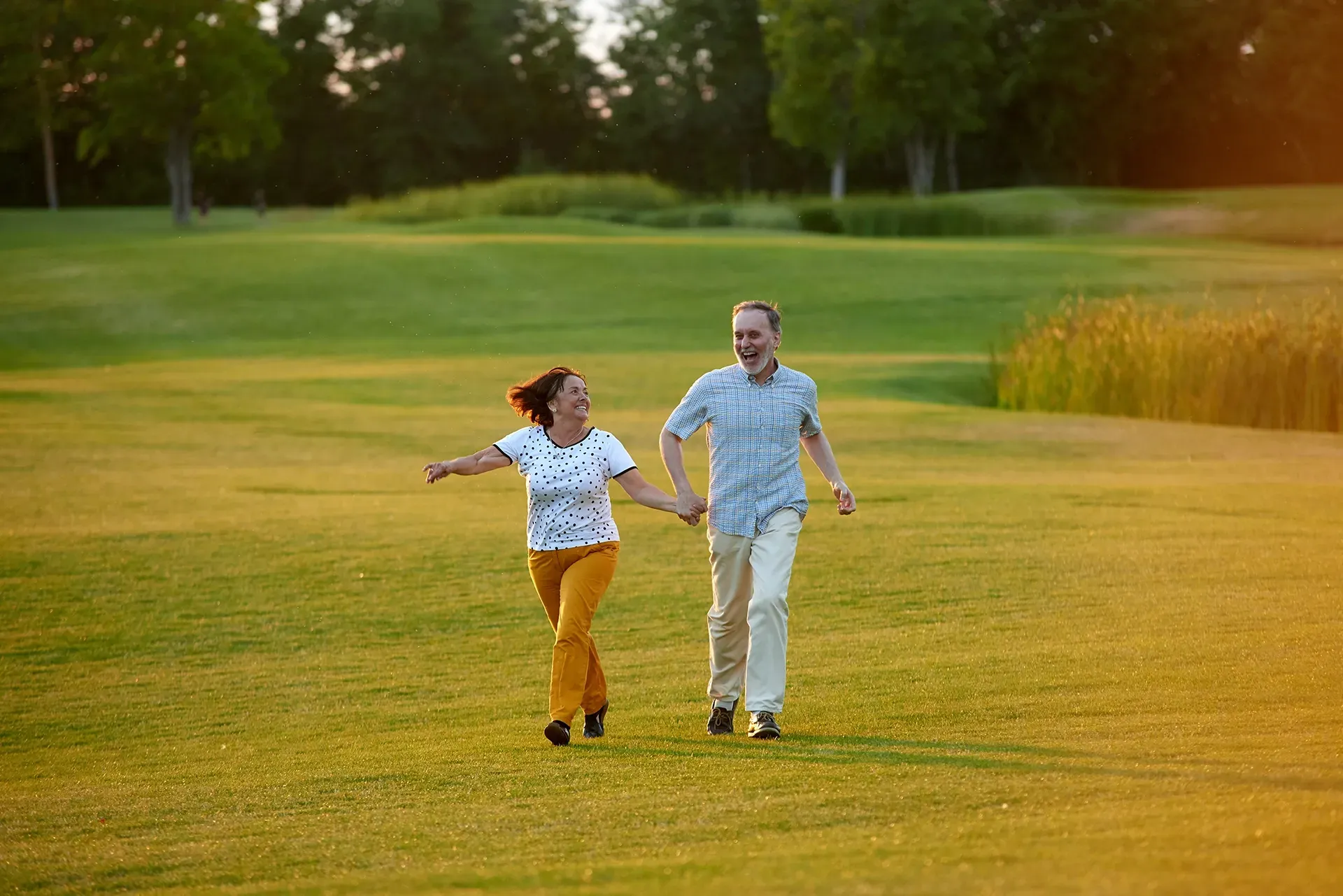 Ein Mann und eine Frau halten sich an den Händen und rennen durch eine Wiese.