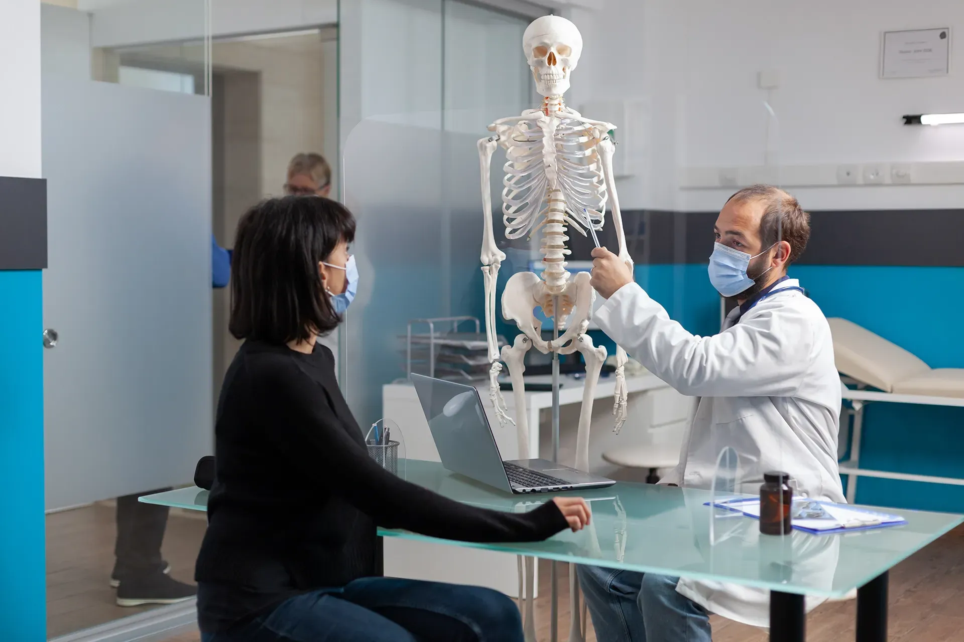 Ein Arzt spricht mit einem Patienten, während er ein Skelett hält.