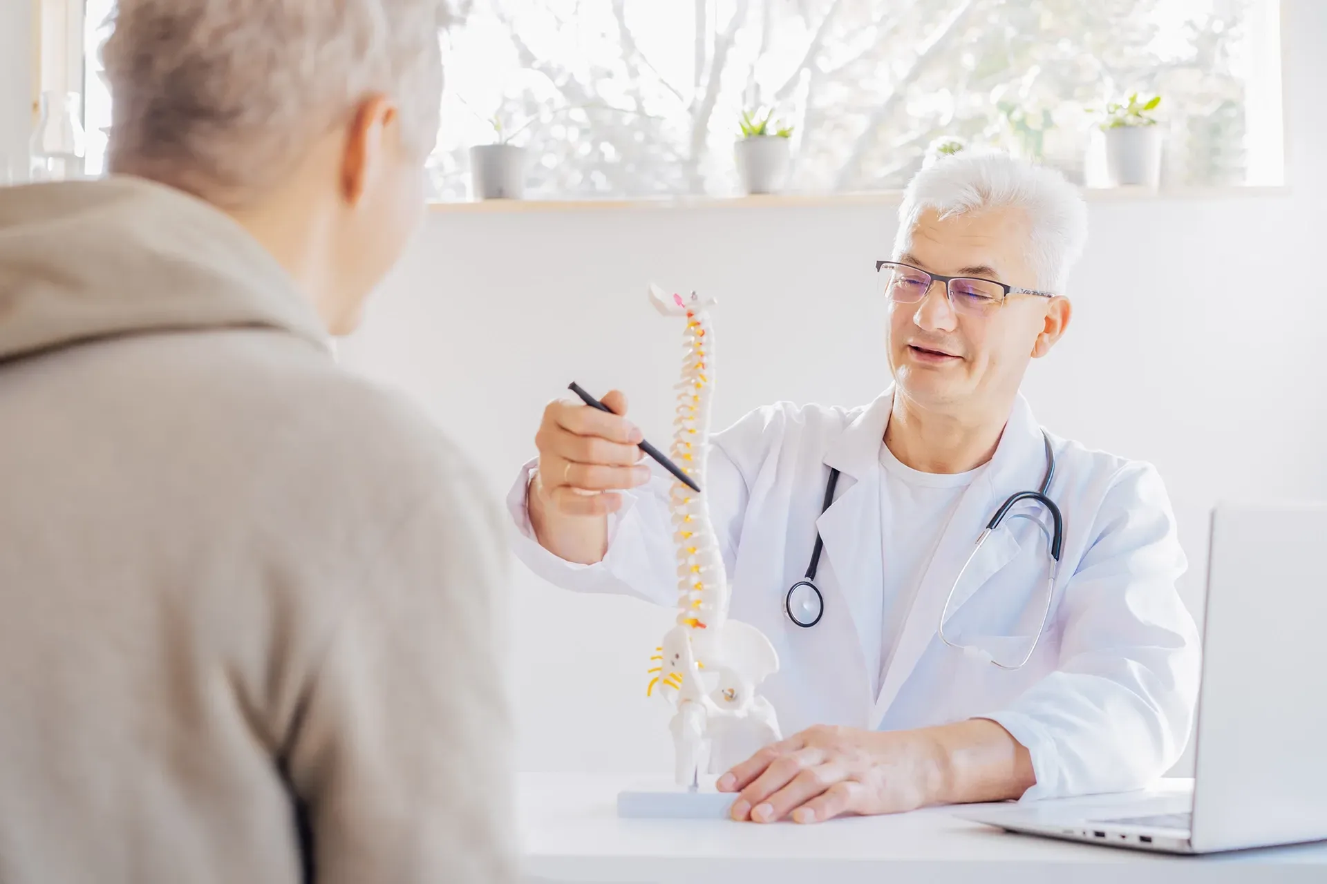 Ein Arzt spricht mit einem Patienten, während er ein Wirbelsäulenmodell in der Hand hält.