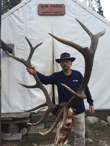 A man holding a large deer antlers in front of a sign that says kim creek