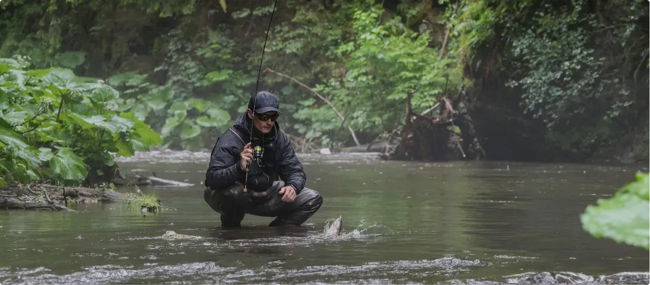 A man is kneeling in a river holding a fishing rod.