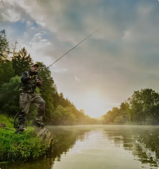 A man is standing on a rock fishing in a lake.
