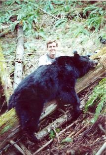 A man standing next to a black bear in the woods