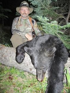 A man is sitting on a log next to a black bear.