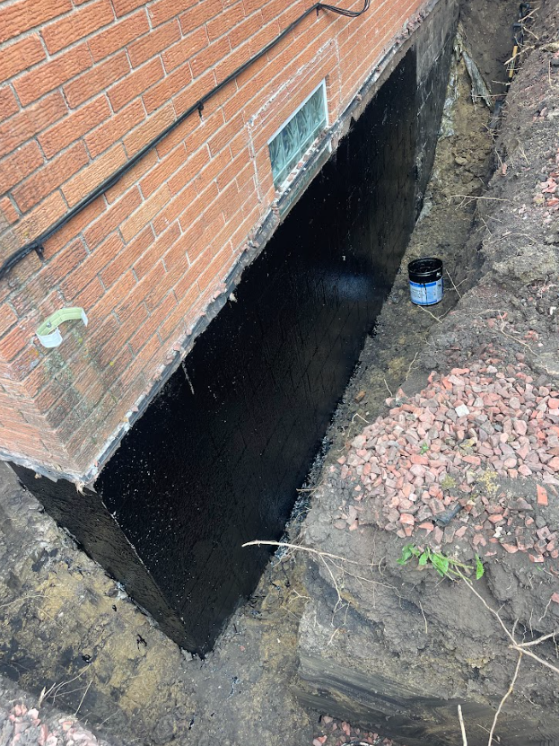 A man is kneeling down in a basement looking at a puddle of water on the floor.