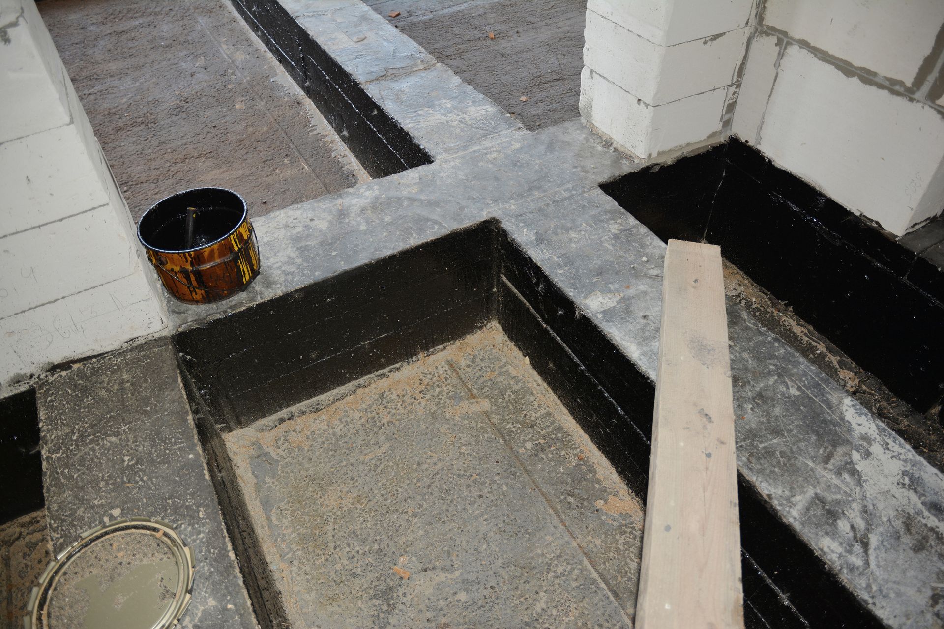 A bucket of cement is sitting on the floor next to a wooden plank.