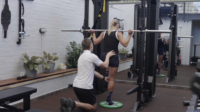 Person receiving leg support during a squat in an outdoor gym area
